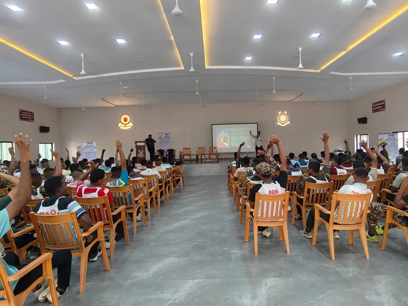 A hall of seated personnel with hands raised during a financial literacy session